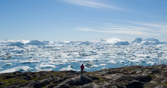 Travel wanderlust adventure in Arctic landscape nature with icebergs - tourist person looking at view of Greenland icefjord - aerial video. Man by ice and iceberg, Ilulissat Icefjord.