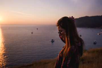 Fototapeta premium Summer sunny lifestyle fashion portrait of young stylish hipster woman walking in mountains, wearing cute trendy outfit, smiling enjoy weekends, travel with backpack. Awesome ocean view on a