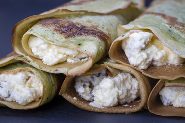 Homemade pancakes with green spirulina stuffed white cottage cheese with raisins on a black slate background, close up