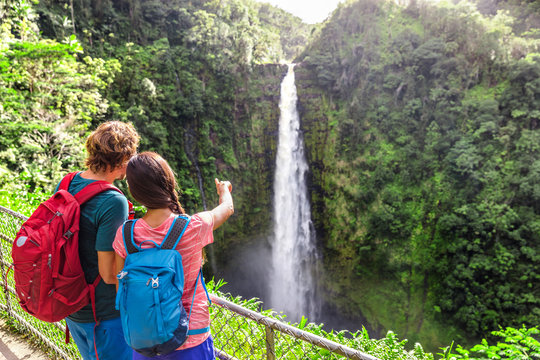 Couple tourists on Hawaii by waterfall. Tourist girl pointing at Akaka Falls waterfall on Hawaii, Big Island, USA. Travel tourism young people concept.