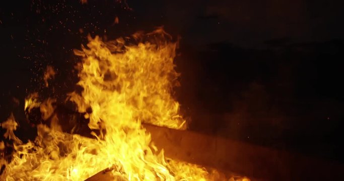 Man throwing burning log onto bonfire close up - slow motion