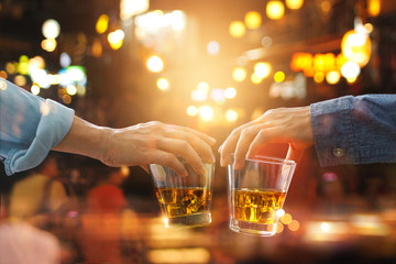 Cheers clinking of friends with bourbon whiskey drinks in party night after work on colorful background