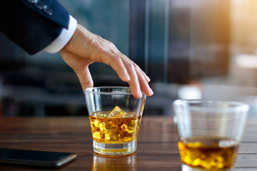 Businessman hand touching bourbon whiskey glass on wooden table in building background