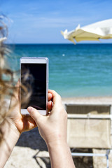 Girl looking at mobile smart phone on a beach with sea on the background. for relaxation and communication concept