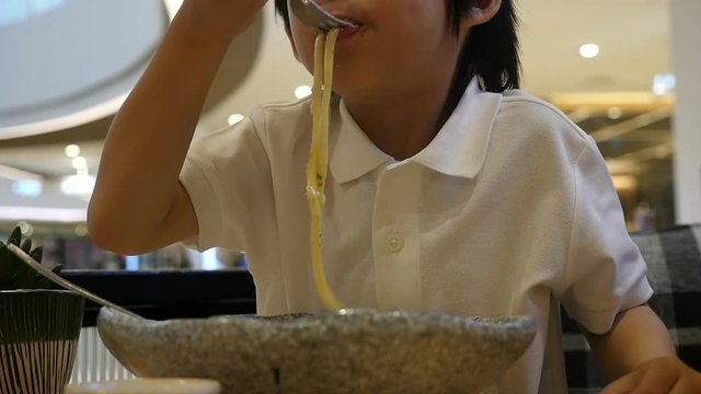 Cute Asian child eating japanese noodles in a restaurant slow motion 