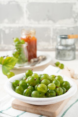 Fresh raw gooseberry berries in  white ceramic plate on light wooden background. Selective focus. Rustic style.