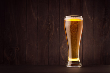 Weizen beer glass with golden sparkling lager on dark wood board, copy space. Template for advertising, design, branding identity, restaurant menu, cover.