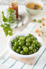 Fresh raw gooseberry berries in  white ceramic plate on light wooden background. Selective focus. Rustic style.