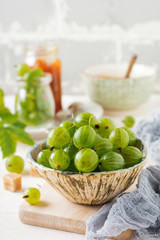 Fresh raw gooseberry berries in  white ceramic plate on light wooden background. Selective focus. Rustic style.