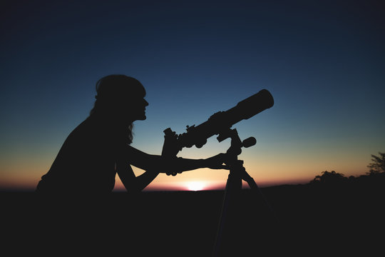 Silhouette of a girl while watching through the telescope.