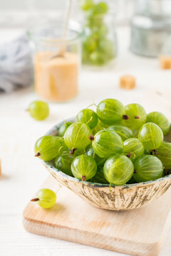 Fresh raw gooseberry berries in  white ceramic plate on light wooden background. Selective focus. Rustic style.