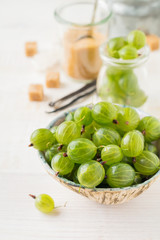 Fresh raw gooseberry berries in  white ceramic plate on light wooden background. Selective focus. Rustic style.