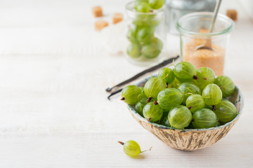 Fresh raw gooseberry berries in  white ceramic plate on light wooden background. Selective focus. Rustic style.