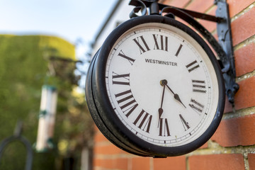 Westminster antique looking station clock attached to a brick wall in a traditional English garden