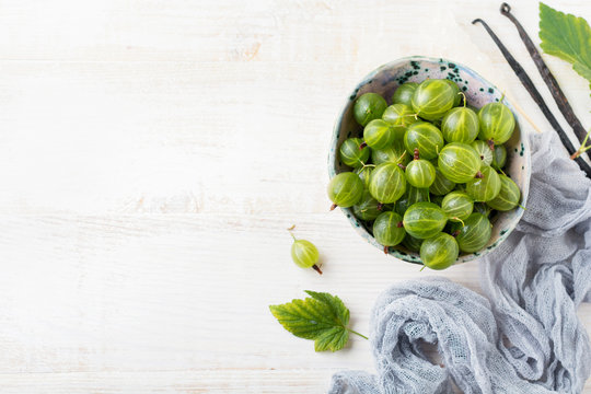 Fresh raw gooseberry berries in  white ceramic plate on light wooden background. Selective focus. Rustic style.top view.