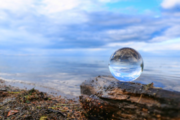 Transparent glass ball on a log reflecting calm blue water of a lake