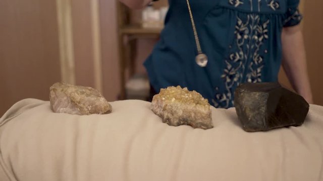 Over the crystals on a mature woman&rsquo;s body an energetic healer is using a crystal pendulum.