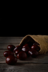 Chestnuts strewing from a bag on a wooden background in dark tones with a leaf with a very high color