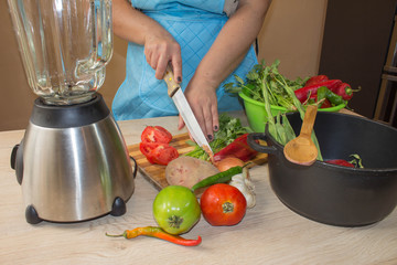 Young woman cooking healthy meal in the kitchen. Cooking healthy food at home. Woman in kitchen preparing vegetables. Chef cuts the vegetables into a meal