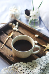 Cup of homemade cocoa with marshmallow, chocolate, flowers and smartphone on rustic wooden tray in the cozy bed