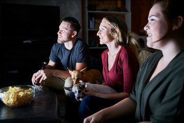 group of three friends watching tv on couch at night eating potato chips