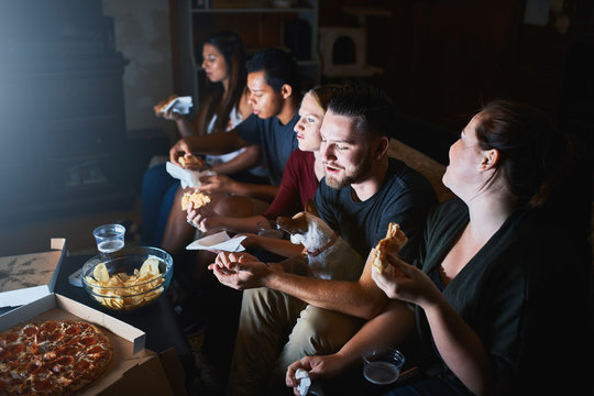 Group Of Friends Watching Tv At Night And Eating Pizza Together