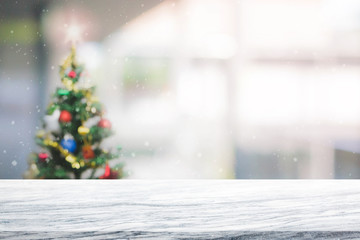 White marble stone table top on blur with bokeh christmas tree background with snowfall - can be used for display or montage your products
