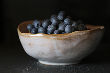 Blueberry . ripe blueberries in a  gray clay cup on a black background. Dark Key. The harvest of blueberries