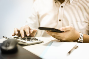 Businessman hand working with finances about cost and calculator and notebook computer with mobile phone in modern office.