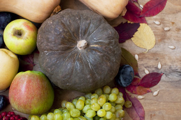 Rural wooden background with autumn fruits and vegetables, bright leaves, pumpkin, grapes, plum, apple, top view. Autumn background.