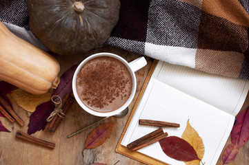 Rural wooden background with pumpkin and autumn leaves, a cup of pumpkin latte with coffee or cocoa, a notebook, a plaid in a cage, top view. Autumn background.