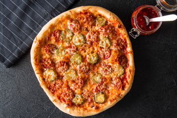 Cut into slices delicious fresh pizza with  pepperoni on a dark background. Top view . Pizza on the black table.