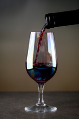 Pouring red wine into the glass against rustic background