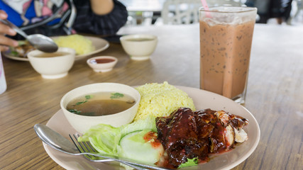 chicken rice,  malaysian food with cucumber slice,salad and soup on wooden table with a glass of chocolate iced