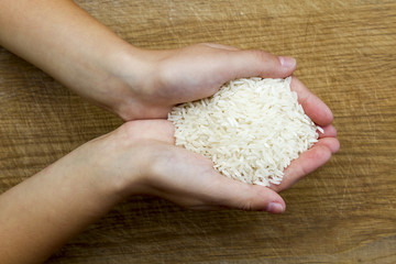 Woman hands holding pile of white raw rice, which is traditional food in eastern culture, over brown wooden background