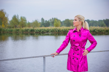 Sweet and cute woman in a pink coat walks in the city park. Bright and interesting elements of the look in the modern style for autumn and spring