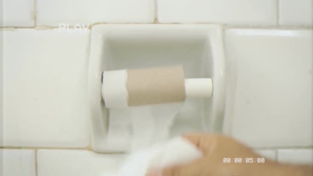 Fake VHS tape: someone grabs the last strip of paper from a toilet roll; it's too short, useless, what a bad surprise. Extreme close-up shot.
