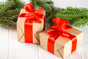 Craft gift boxes with red ribbon and bow, green Christmas tree, decorations, on white wooden background. Xmas and New Year congratulation card, banner, flyer.