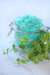  mint bath salt.  green salt with mint extract in a glass jar and twigs of fresh mint on a wooden light gray background. organic natural cosmetics concept.