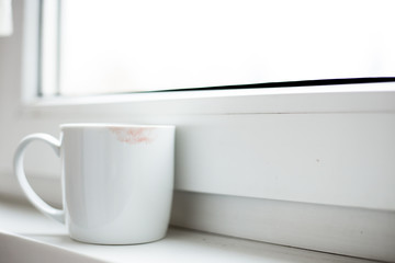 cup with lipstick near window on white background