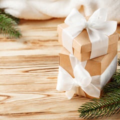 Craft gift boxes with white ribbon, bow, green Christmas tree, decorations, white plaid on wooden background. Xmas and New Year congratulation card, banner, flyer.