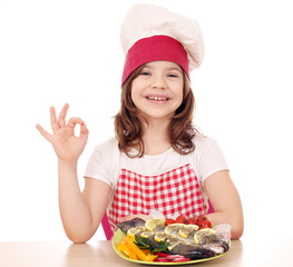 happy little girl cook with trout on plate and ok hand sign