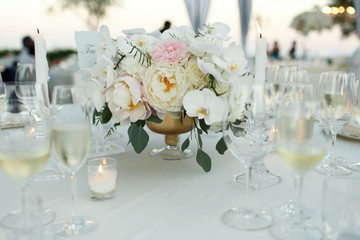 Tender bouquet of orchids and peonies stands in the middle of dinner table