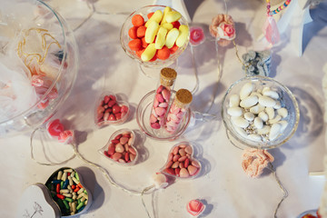 Glass bowls with colorful chocolate pills stand on wedding candy bar