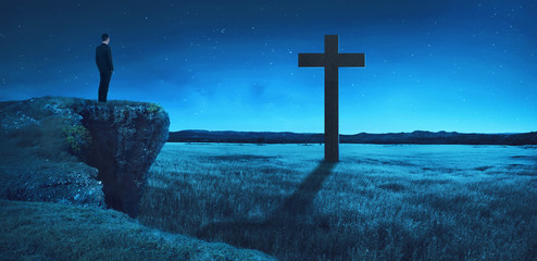 Man standing on the top of the cliff looking to the cross