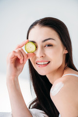 woman holding slice of cucumber on eye