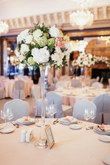 Tall vase with white and green flowers stands on round dinner table number nine