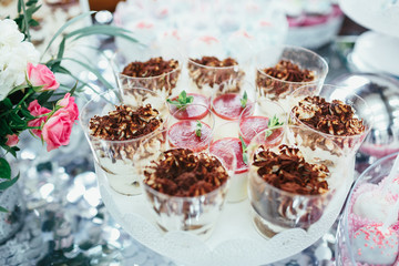 Cups with cold desserts with strawberry stand on plate on silver table