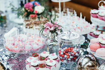 Candy bar covered with silver cloth and served with pink sweets and flowers