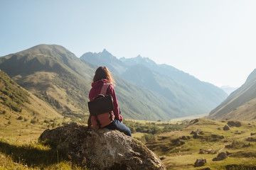 a young woman traveler with backpack enjoying view of autumn mountains, rear view